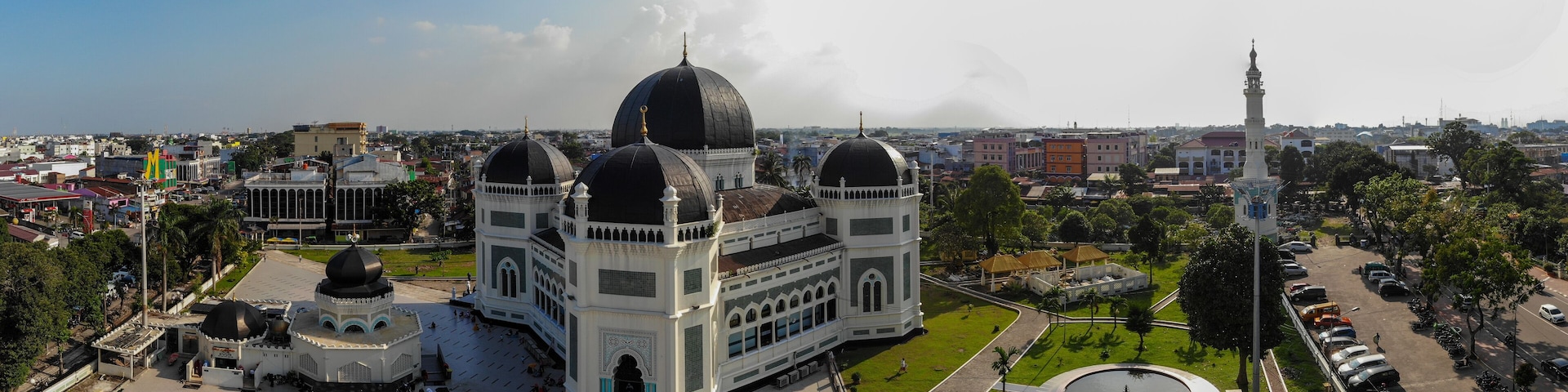 A large mosque with multiple domes and a minaret, surrounded by a spacious courtyard and greenery.
