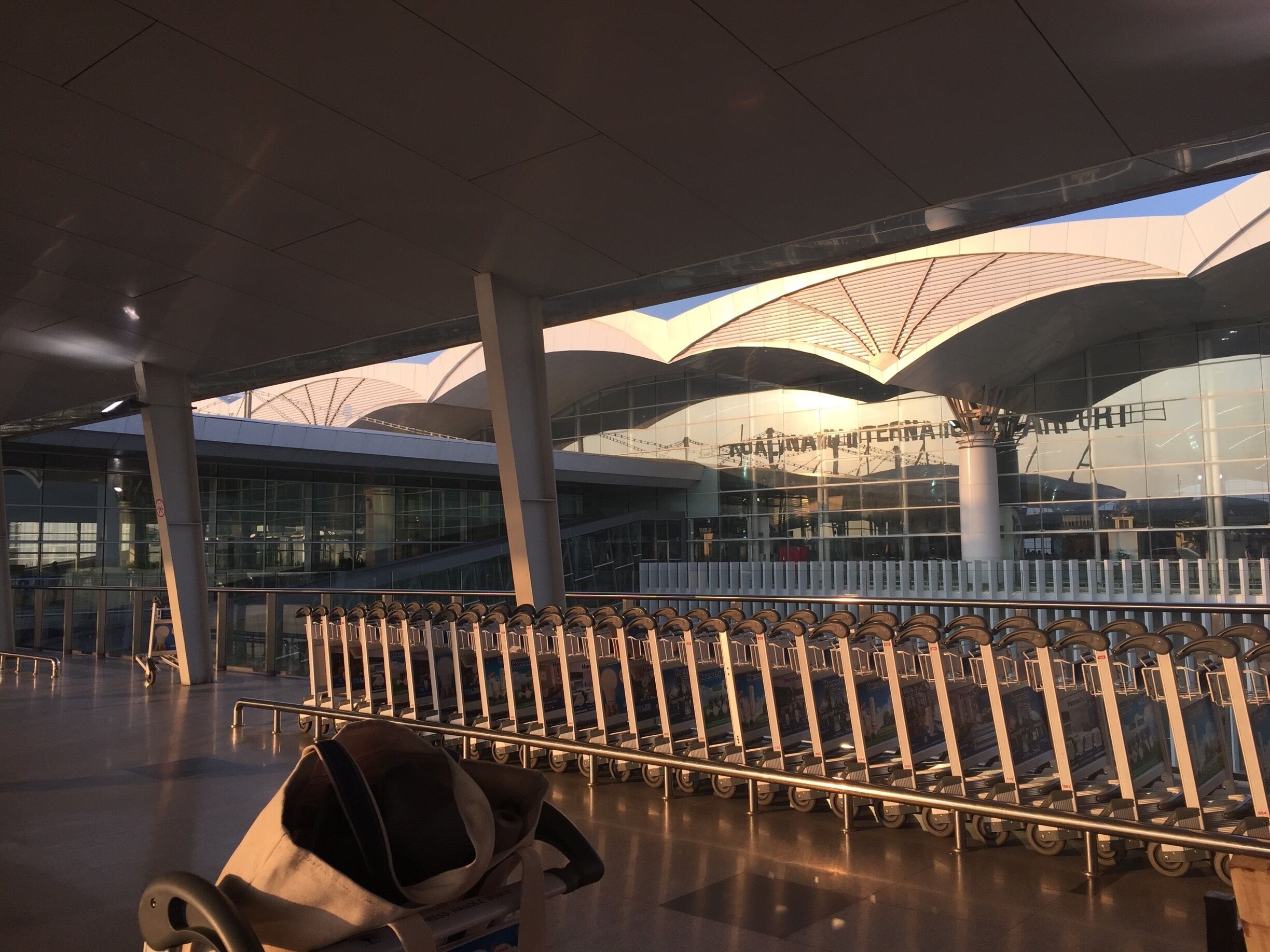 Um terminal aeroportuário moderno com fachada de vidro, fileiras de carrinhos de bagagem e um design de teto marcante.