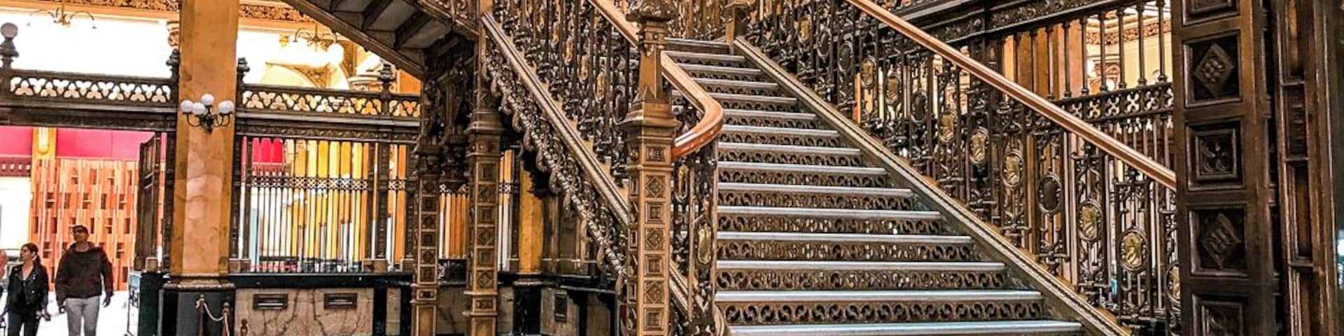 Una imponente escalera ornamentada con barandales de metal intrincados y varios descansos, que conduce a un nivel superior.