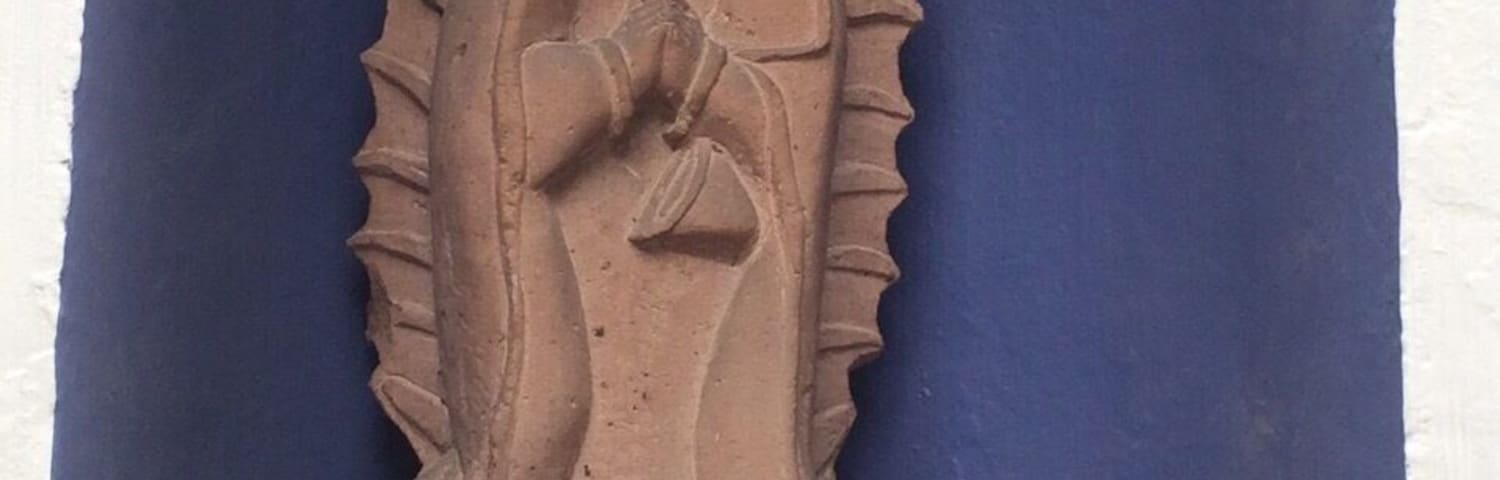 Escultura em pedra de uma figura religiosa com auréola, ao fundo de uma parede azul.
