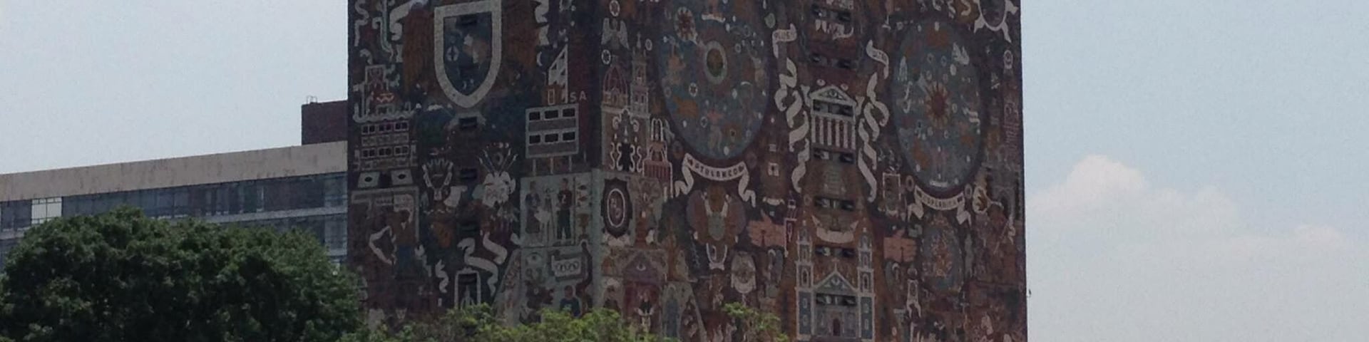 Ein Gebäude mit Wandgemälde verschiedener Kultursymbole und einer Menschenmenge in einem Park.