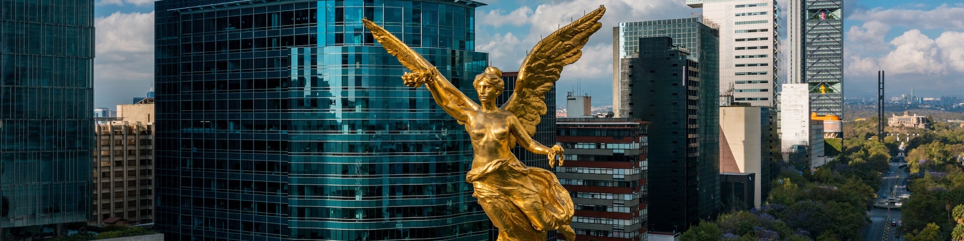 Una estatua dorada de un ángel, modernos rascacielos y una calle bordeada de árboles.