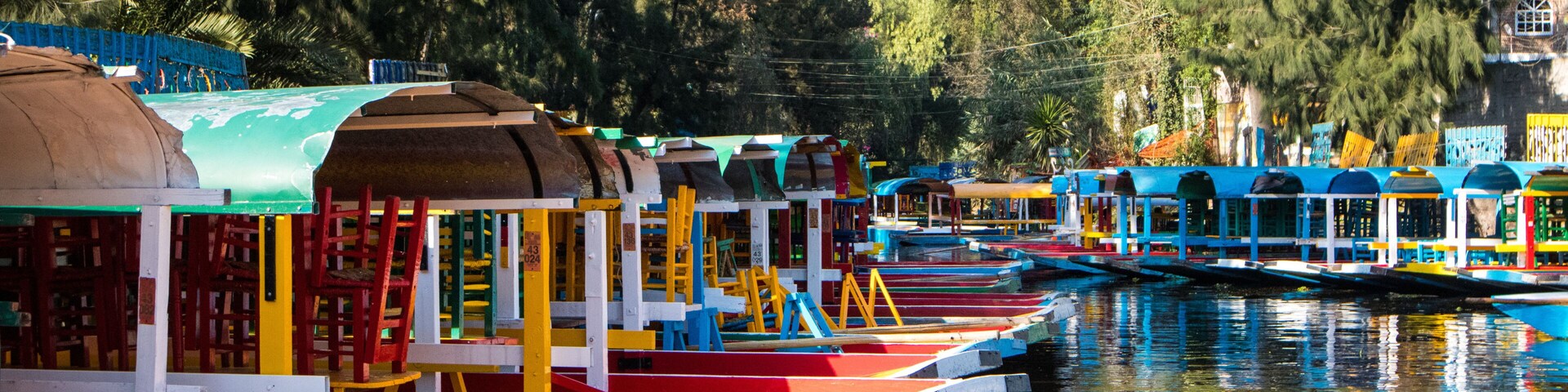 Botes coloridos amarrados a orillas de un río, rodeados de árboles y edificios.