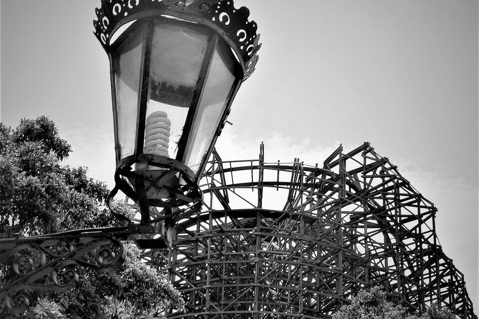 A black and white amusement park with a roller coaster and a vintage street lamp.