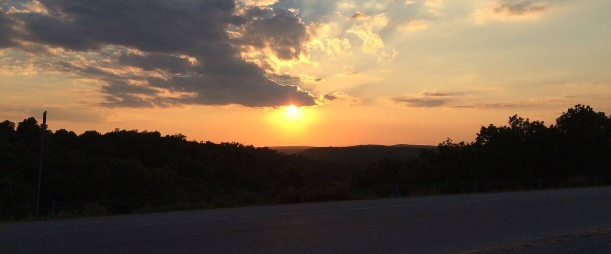 A sunset over a road with trees in the background.