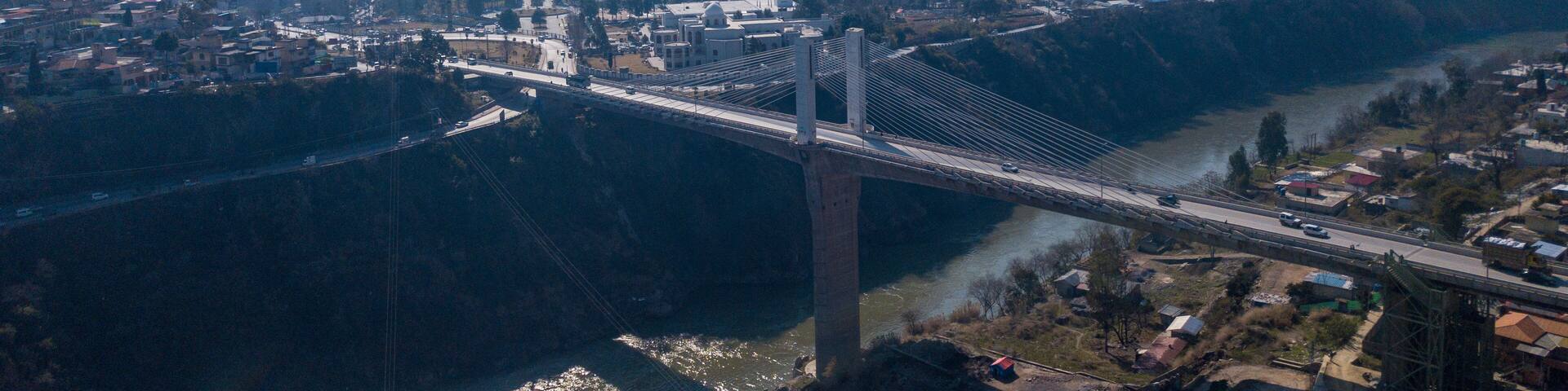 Aerial view of the earth quake memorial bridge spanning a river amidst scenic mountains and a vibrant valley, Muzaffarabad, Azad Jammu Kashmir, Pakistan.