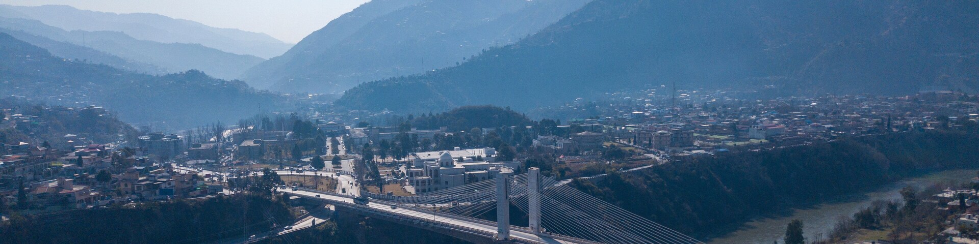 Aerial view of the earth quake memorial bridge spanning a river amidst scenic mountains and a vibrant valley, Muzaffarabad, Azad Jammu Kashmir, Pakistan.