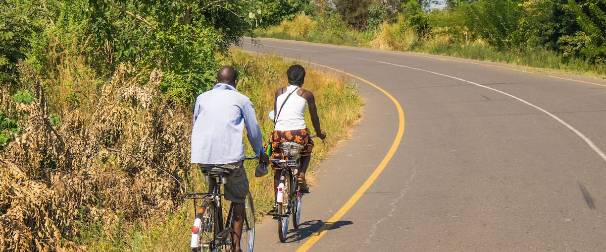 Two people riding bicycles on a curving road surrounded by greenery.