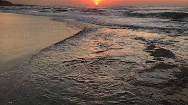 A beach at sunset with waves crashing onto the shore and a clear sky.