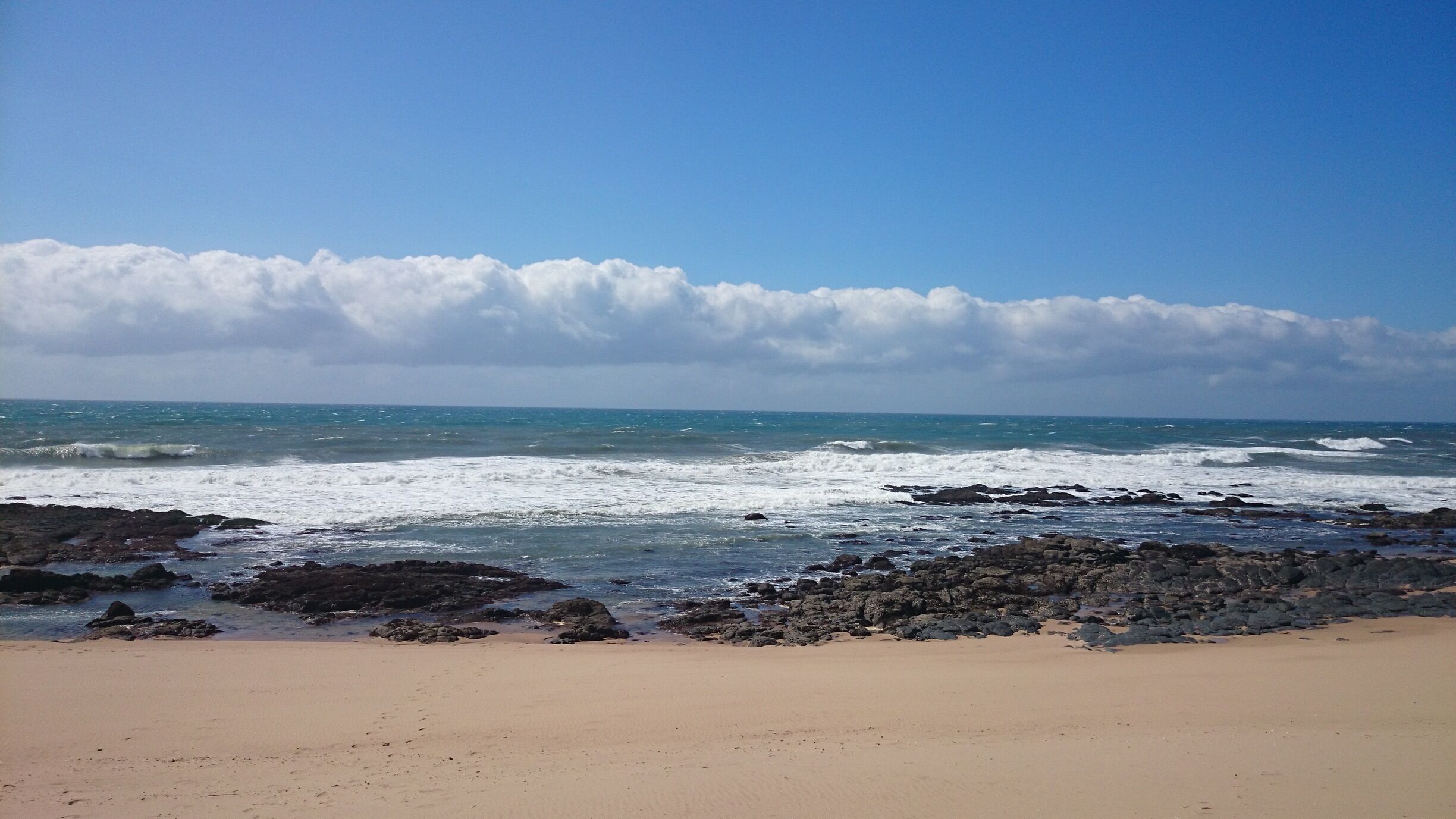 A beach with waves crashing onto rocky shores under a partly cloudy sky.
