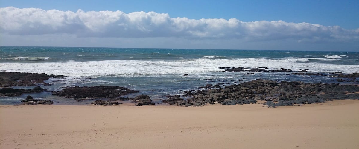 A beach with waves crashing onto rocky shores under a partly cloudy sky.