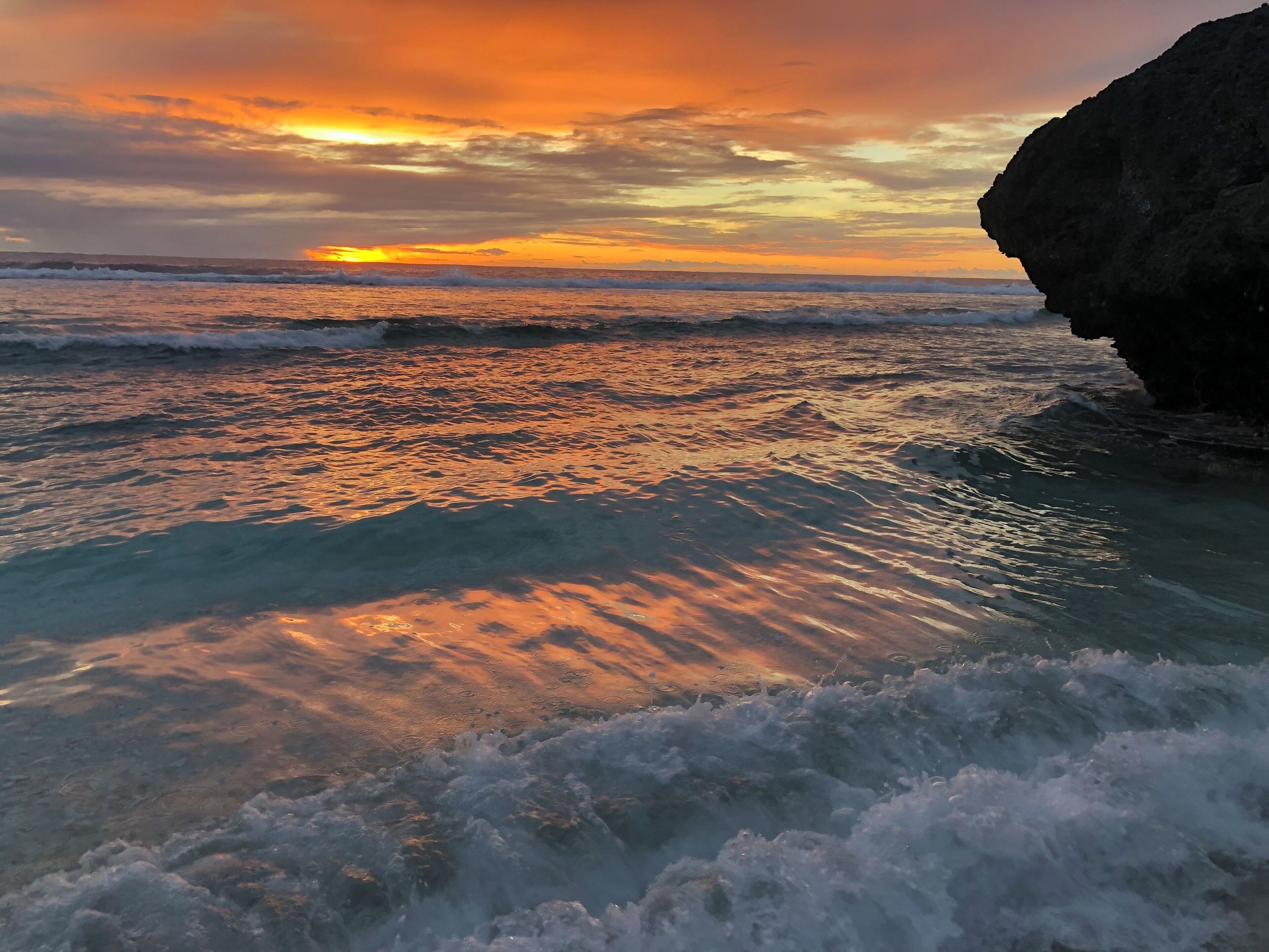 A sunset over a rocky coastline with waves crashing onto the shore.