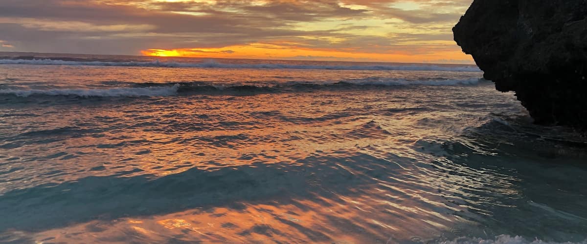 A sunset over a rocky coastline with waves crashing onto the shore.