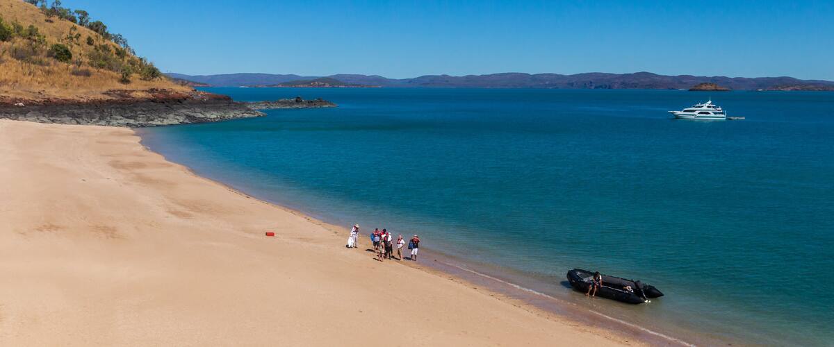 A beach with a group of people, a boat, and distant mountains.