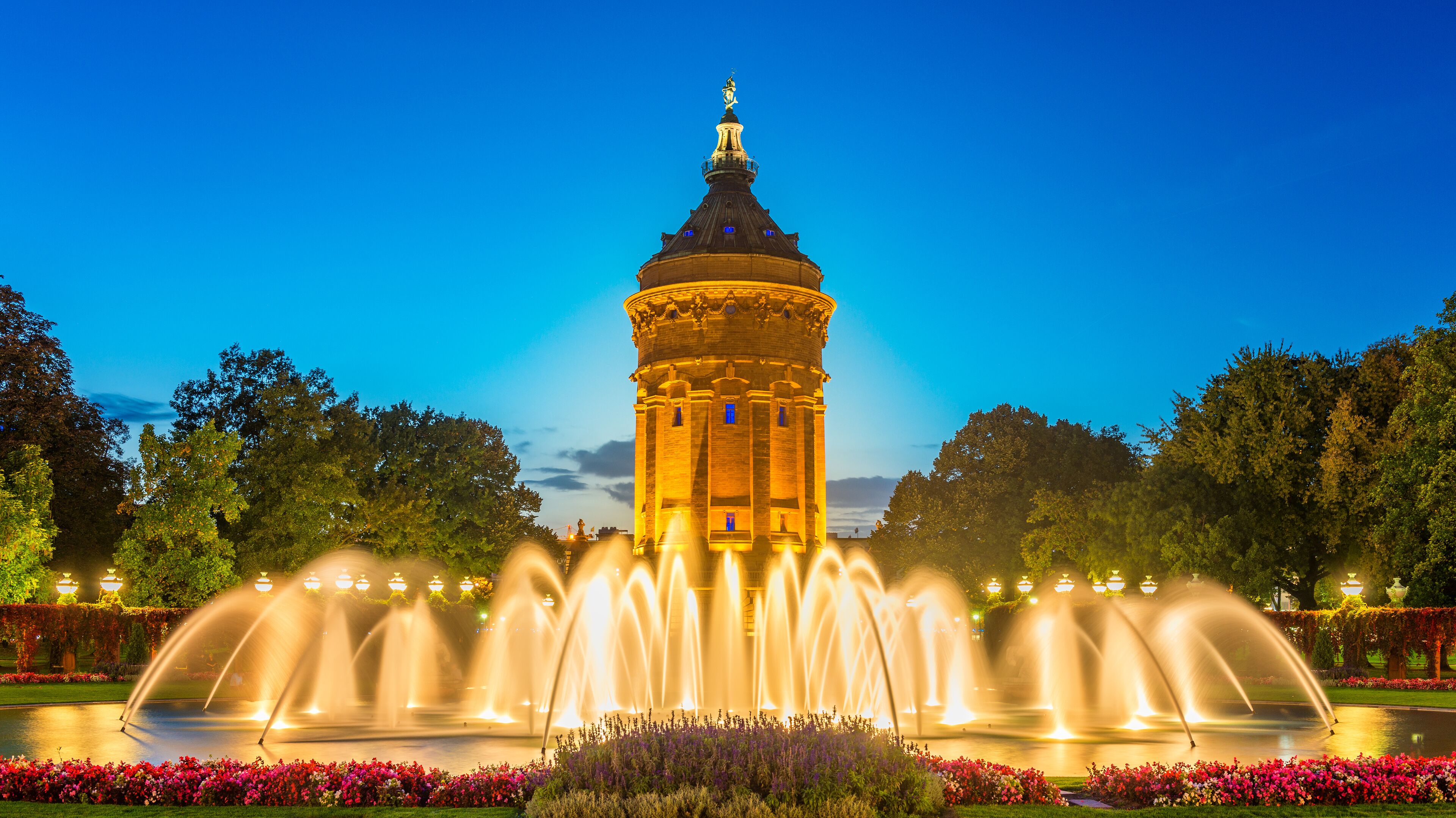 A tower with a statue on top, surrounded by a fountain and colorful flowers.