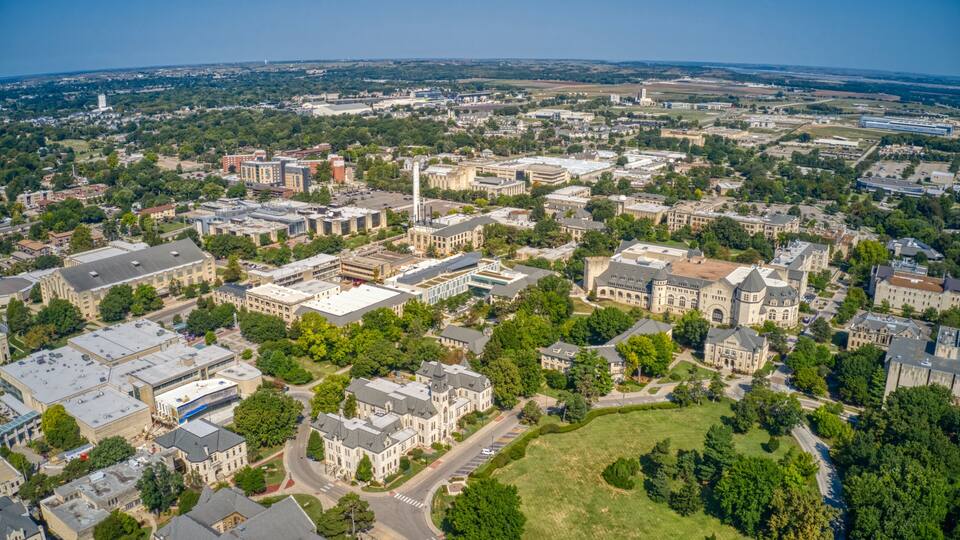 An aerial view of a university campus with historic buildings, green spaces, and a river.