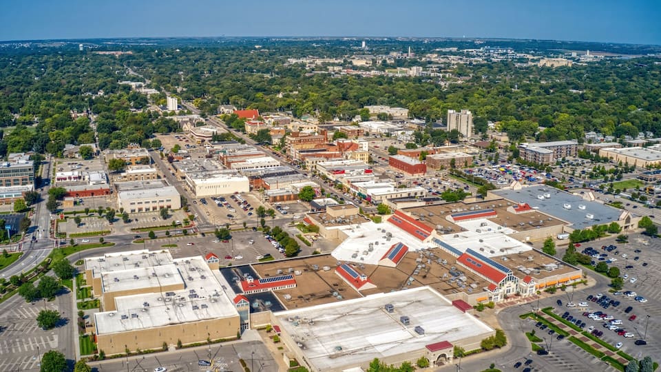 An aerial view of a city with a mix of commercial buildings, parking lots, and green spaces.