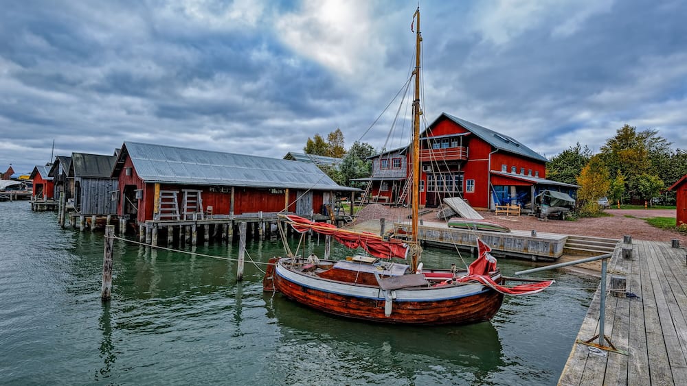 A wooden boat docked at a pier with a red building in the background.