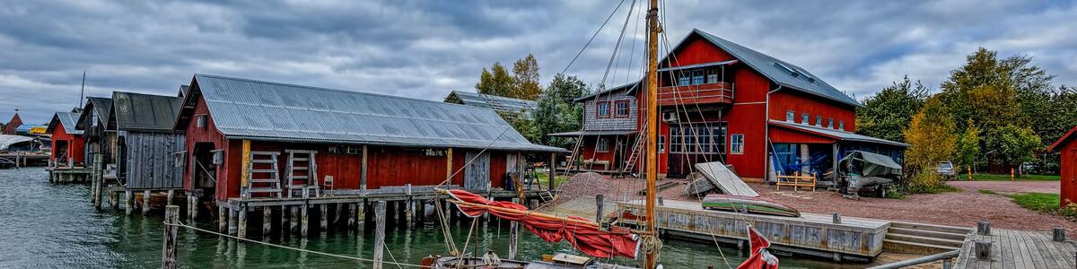 A wooden boat docked at a pier with a red building in the background.