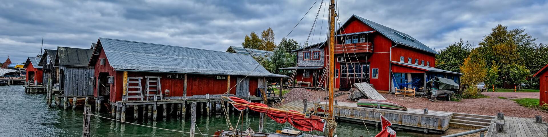 A wooden boat docked at a pier with a red building in the background.