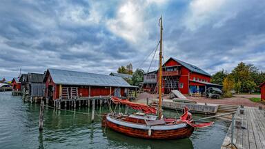 A wooden boat docked at a pier with a red building in the background.