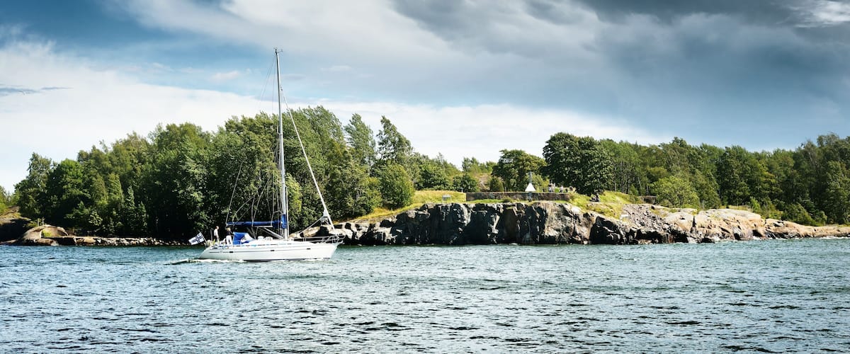 A sailboat on calm waters near a rocky shoreline with dense green trees.