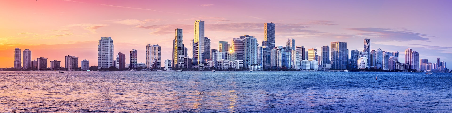 Silhueta urbana com edifícios altos à beira-mar ao pôr do sol.