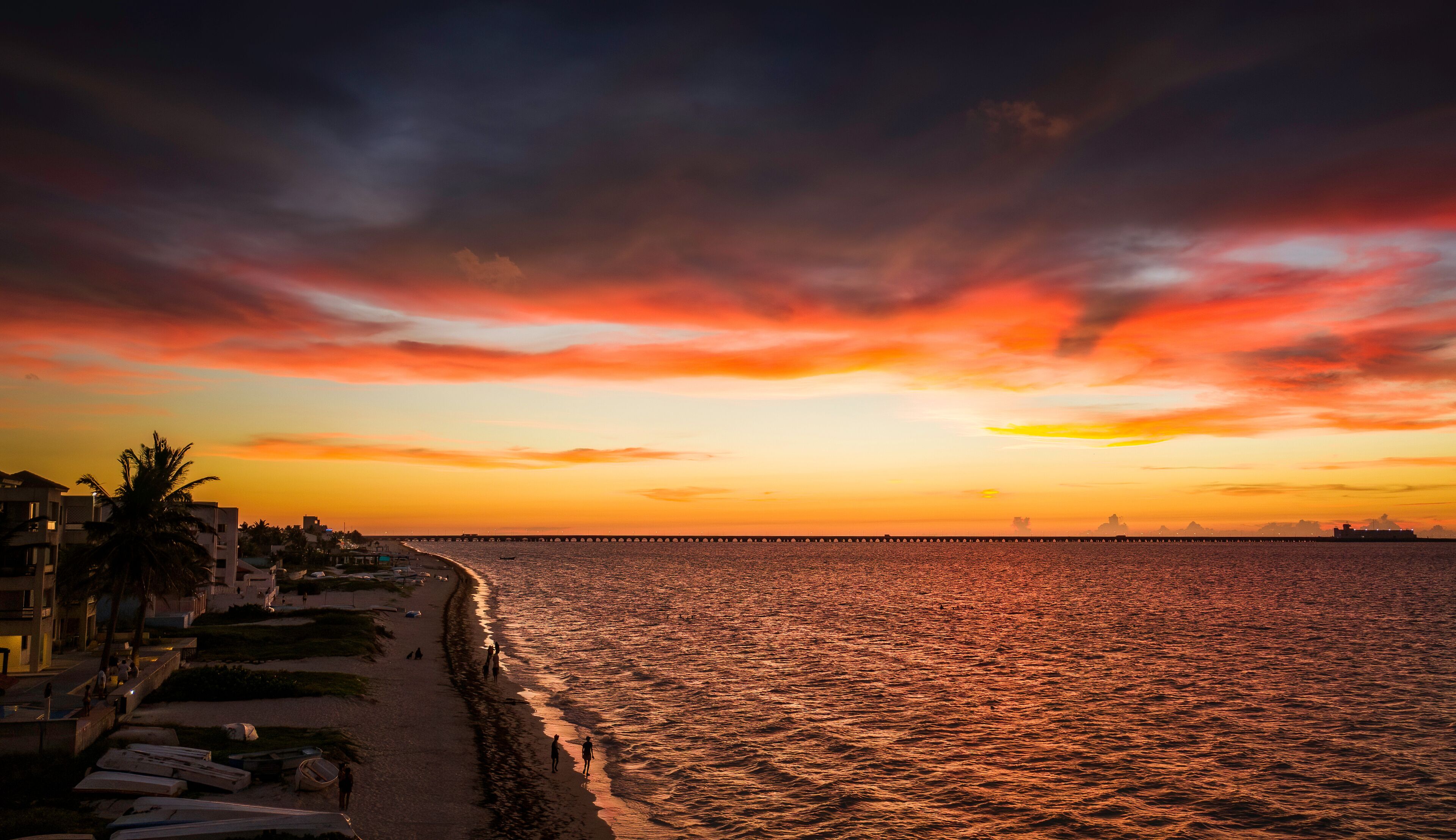 Una playa al atardecer con un muelle que se adentra en el agua.