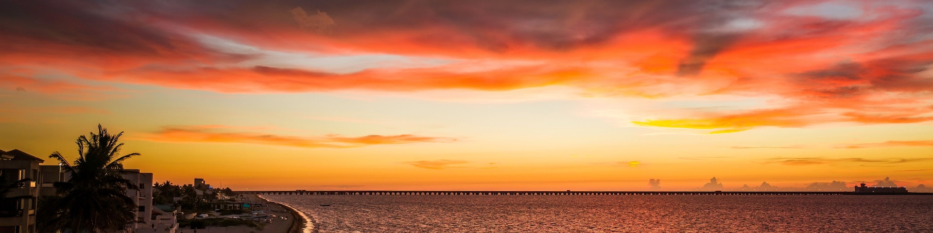 Una playa al atardecer con un muelle que se adentra en el agua.