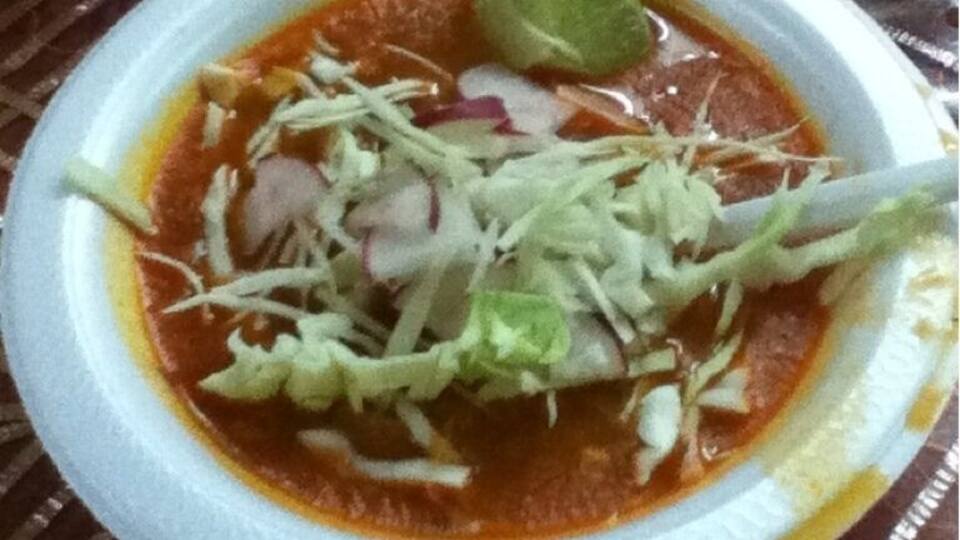 A bowl of soup with shredded lettuce, radish, and lime on a paper plate.