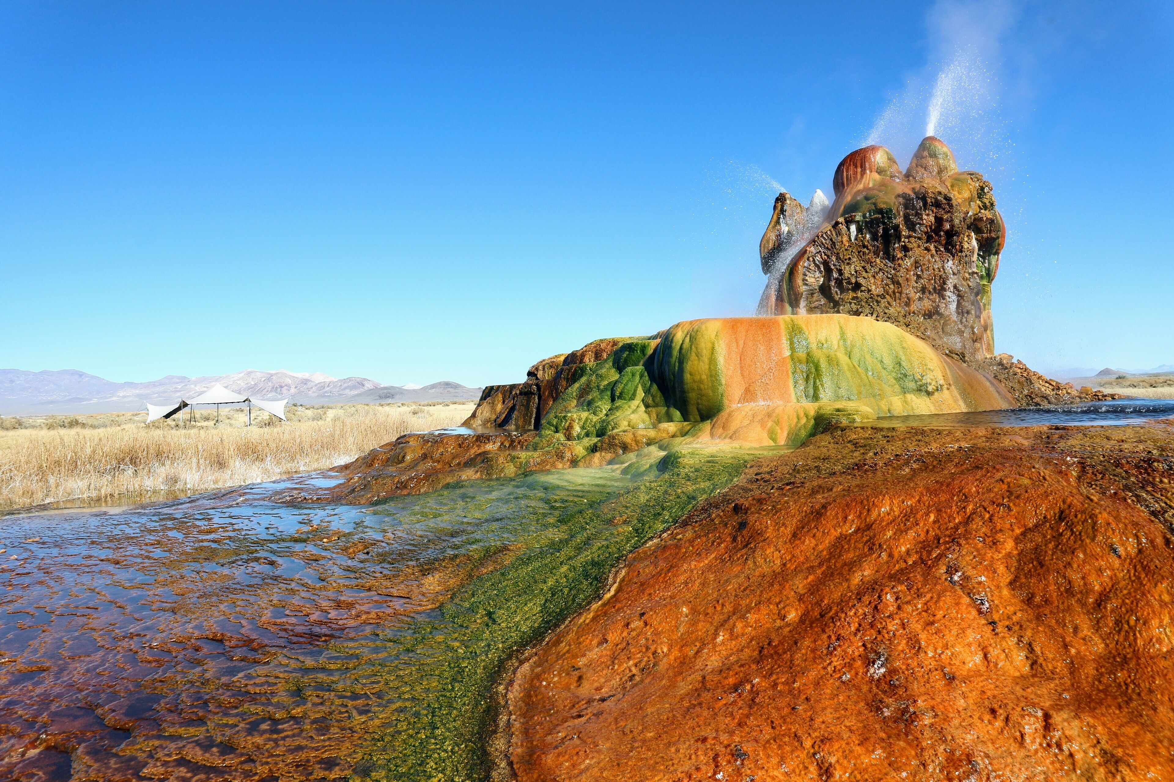A geothermal area with colorful mineral deposits and a geyser.