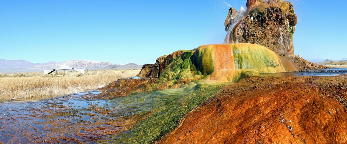 A geothermal area with colorful mineral deposits and a geyser.