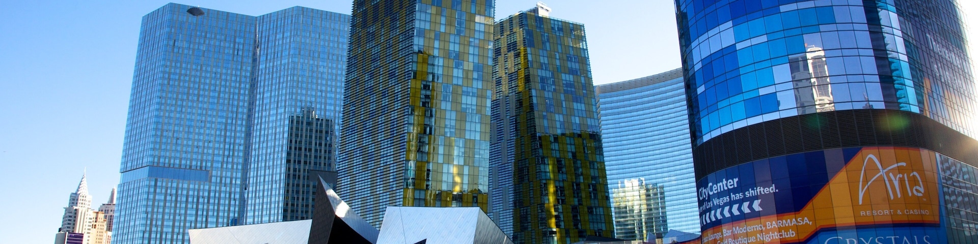 Paisagem urbana com arranha-céus modernos, incluindo um edifício com fachada de vidro refletiva e outro com design geométrico marcante.