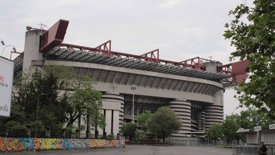 A large stadium with a curved roof and graffiti on the surrounding walls.