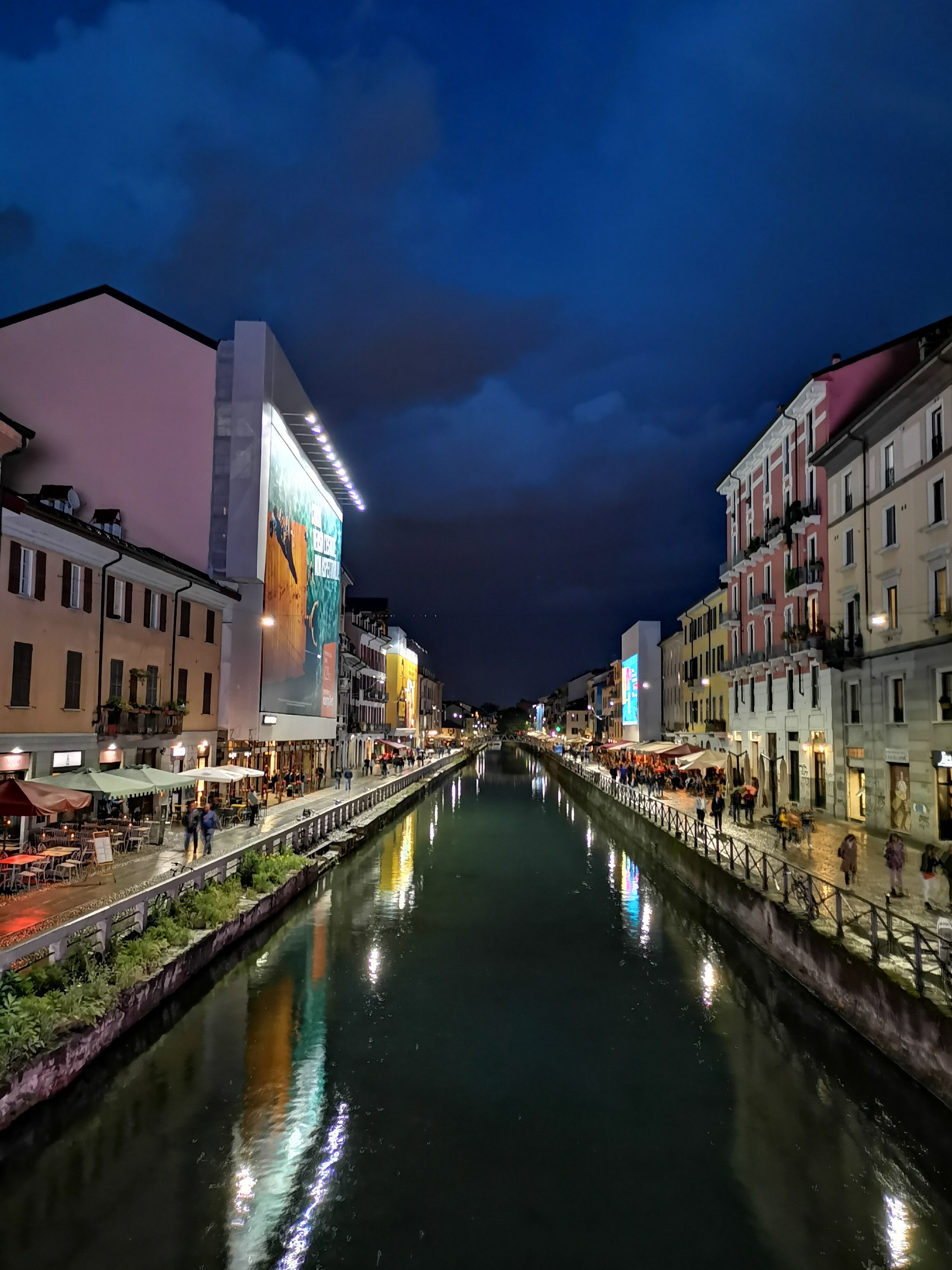 Un canal flanqueado por edificios, un puente y un gran cartel iluminado.