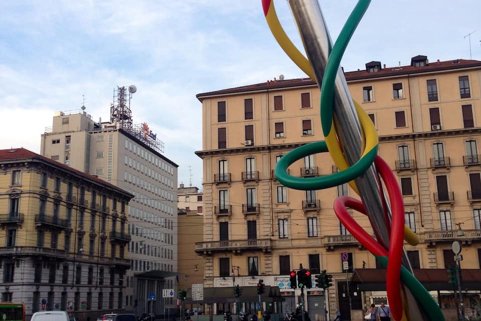 A street with a colorful sculpture, buildings, and traffic signs.