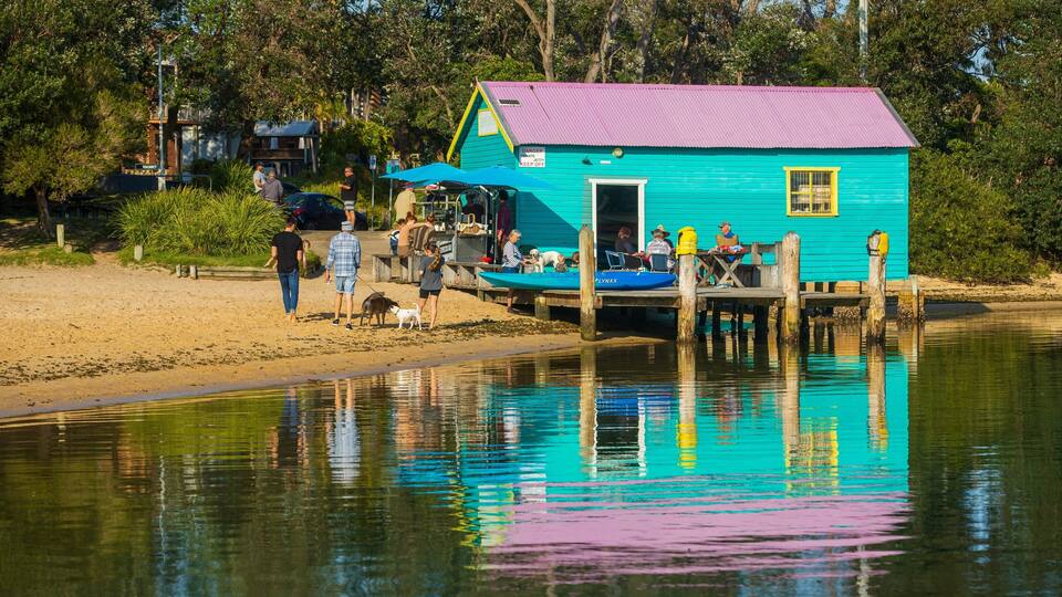 A turquoise house with a pink roof on stilts by a calm lake.
