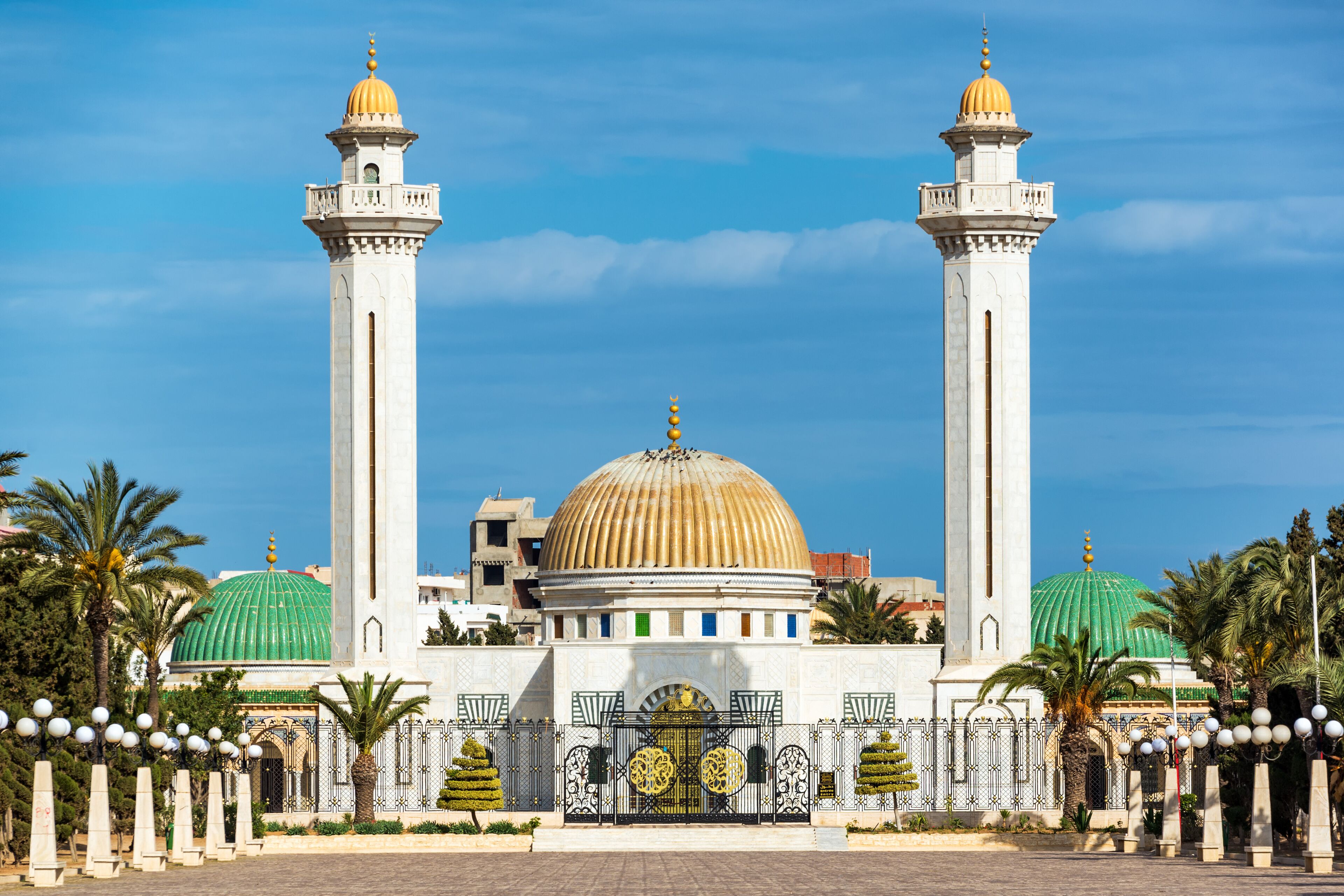 A mosque with two minarets, a large central dome, and a green dome.