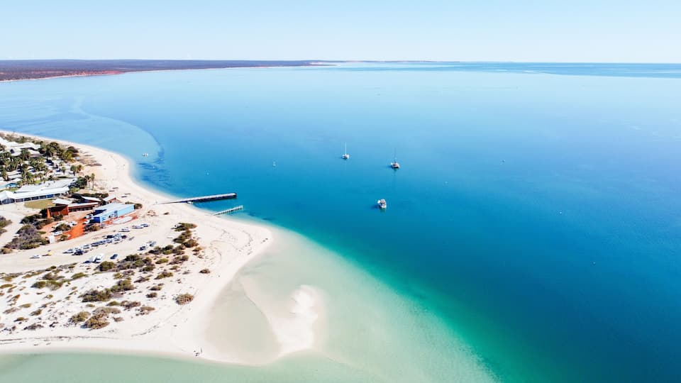 An aerial view of a coastal area with a beach, a pier, and several boats.