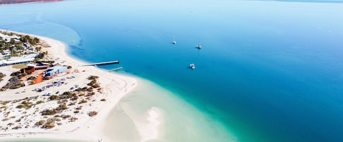 An aerial view of a coastal area with a beach, a pier, and several boats.