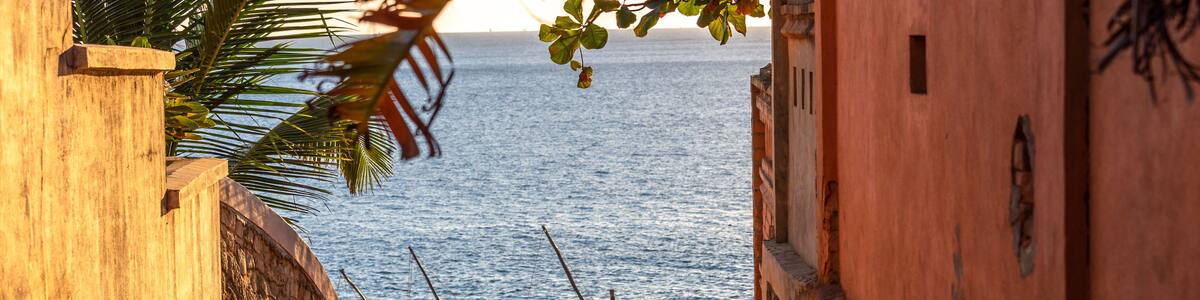 A coastal path with boats and a person sitting on the sand.