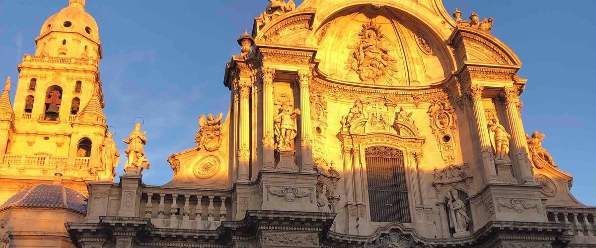 A grand cathedral with intricate sculptures and columns, illuminated by warm evening light.