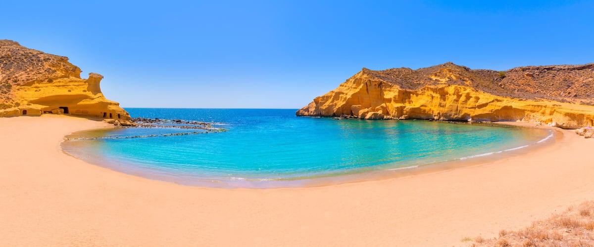 A beach with clear turquoise waters, sandy shore, and rocky cliffs.