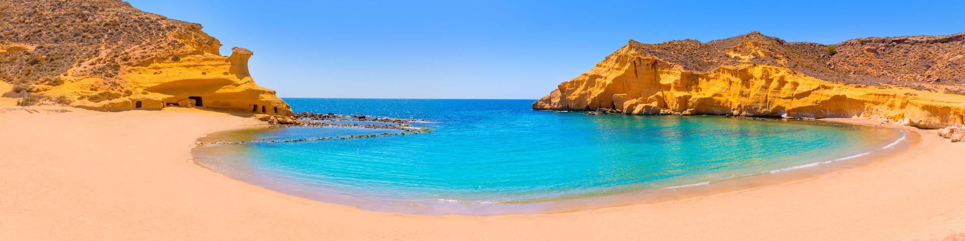 A beach with clear turquoise waters, sandy shore, and rocky cliffs.