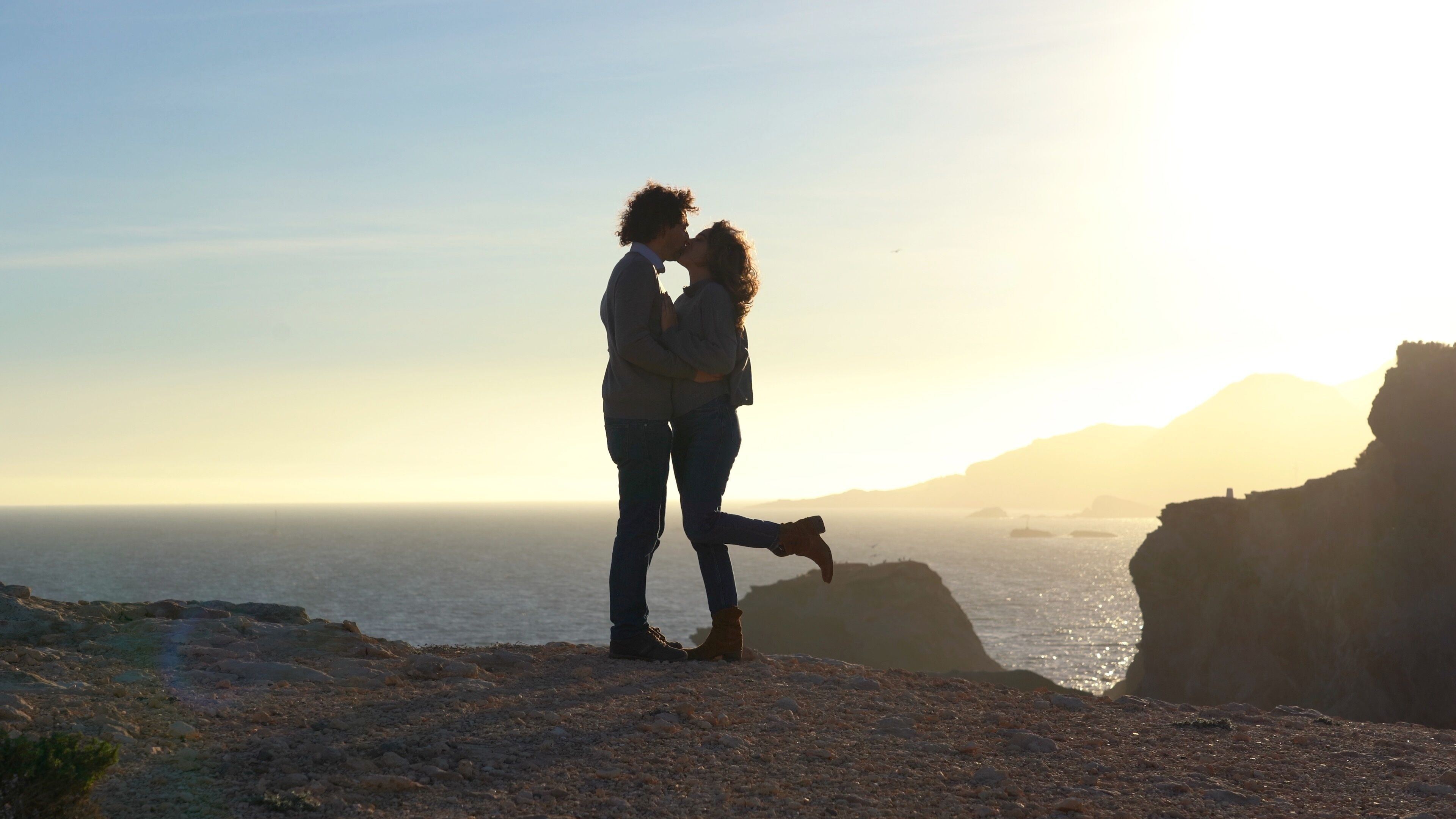 man and woman walk on a cliff by the sea at sunset in total freedom of nature - they spread their arms holding hands, kiss and hug during the journey in Murcia Spain La Manga
