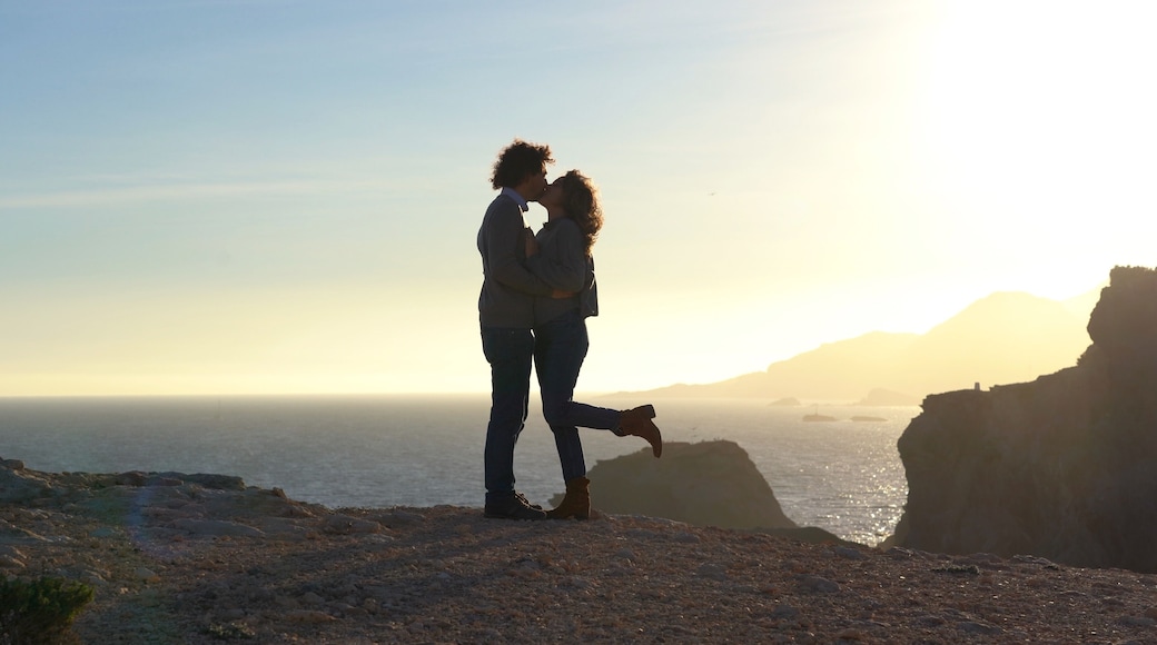 man and woman walk on a cliff by the sea at sunset in total freedom of nature - they spread their arms holding hands, kiss and hug during the journey in Murcia Spain La Manga