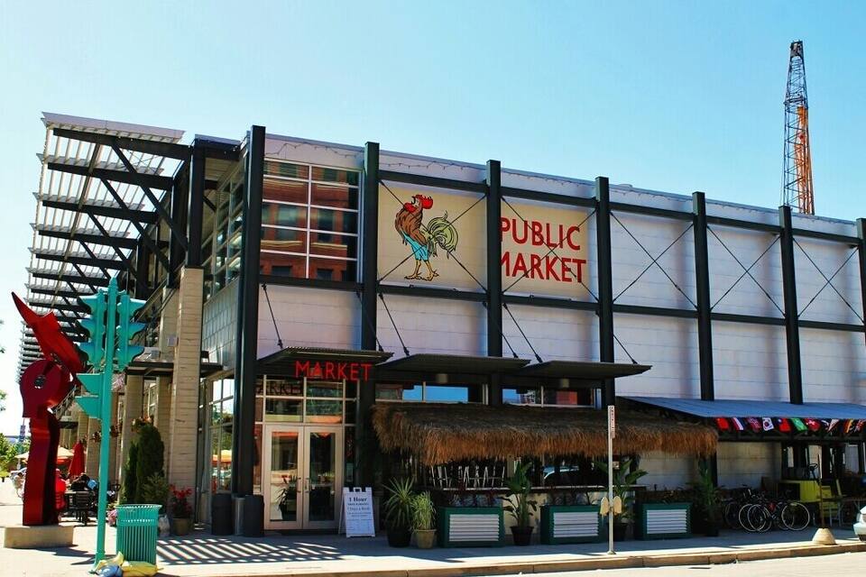 A public market building with a rooster sign, a thatched-roof structure, and a tall tower in the background.