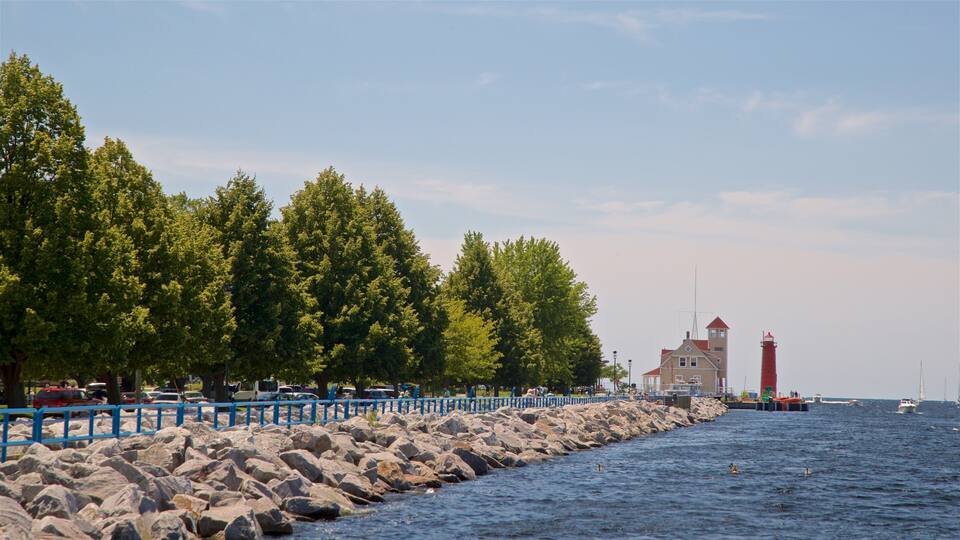 A rocky shoreline with a lighthouse, trees, and boats on the water.