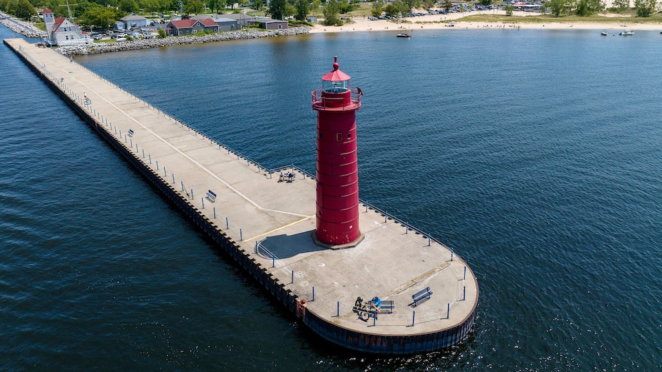 A red lighthouse on a pier extending into a calm body of water.