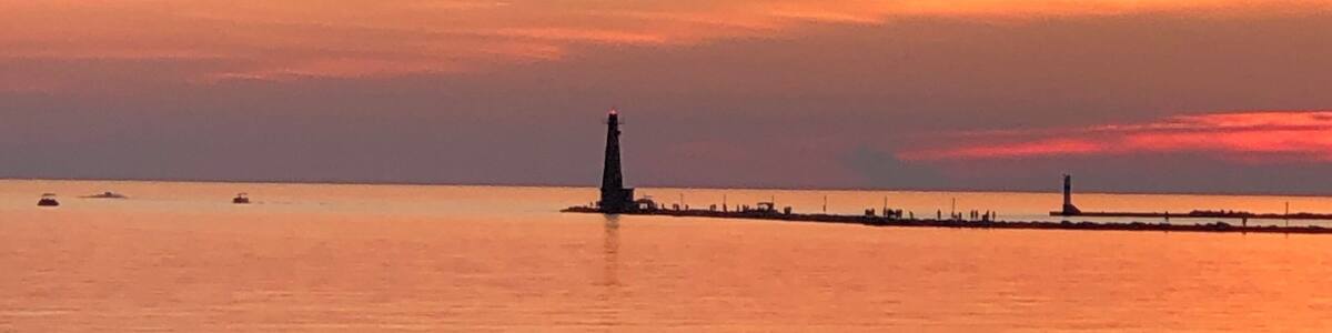 A sunset over a calm sea with a lighthouse and a pier extending into the water.